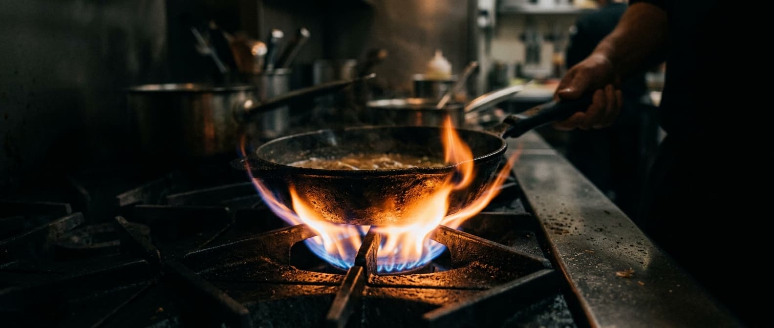 A pan over an open flame in a working restaurant kitchen