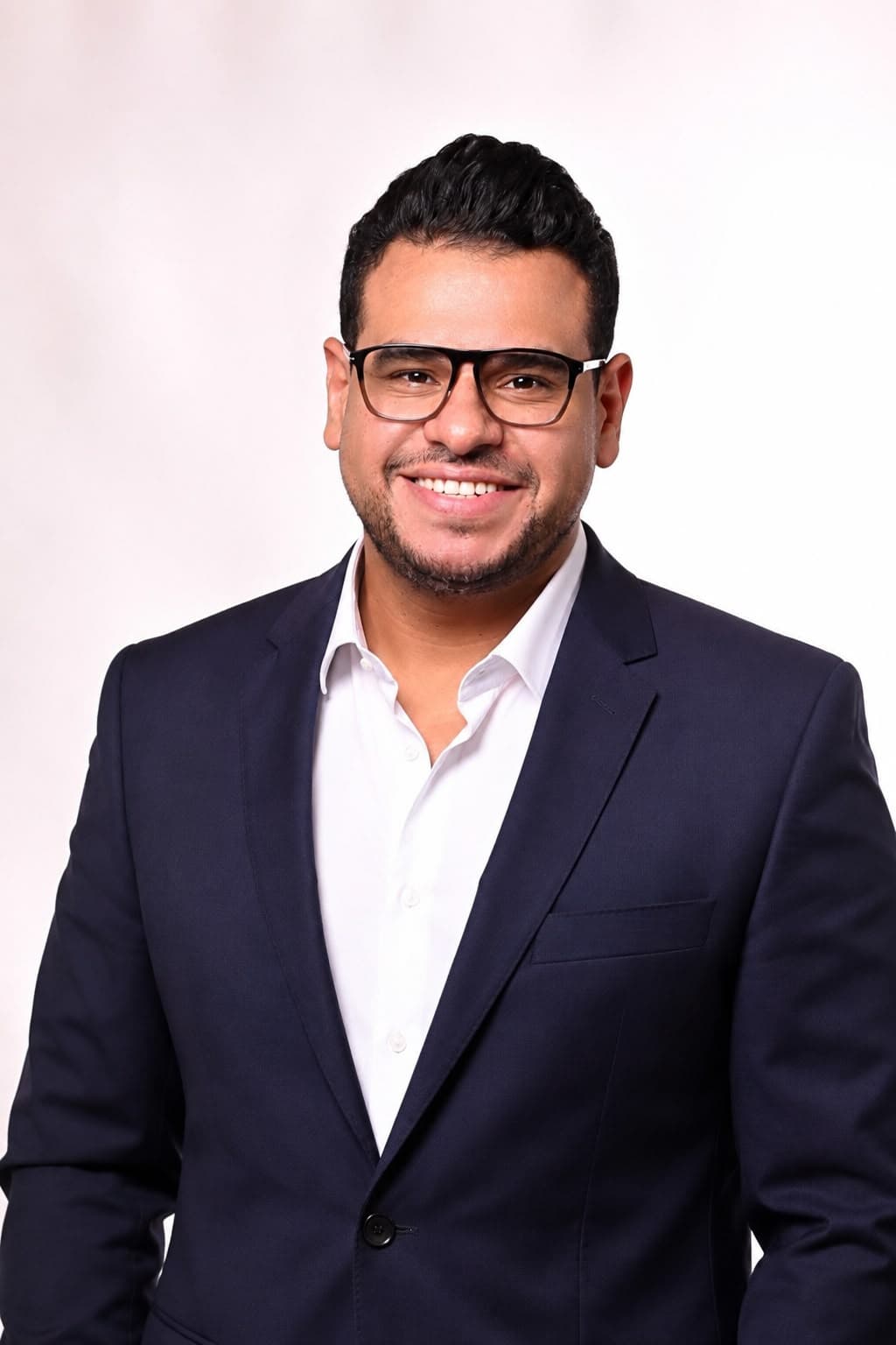 Alaa Mamdouh smiling, in glasses, a navy blazer and white shirt, in a studio portrait