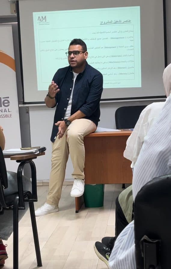Alaa running a session at the front of a training room, slides on the screen behind him