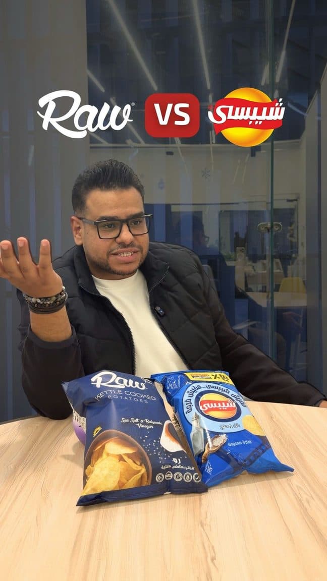 Alaa comparing two packaged products at a table, on camera