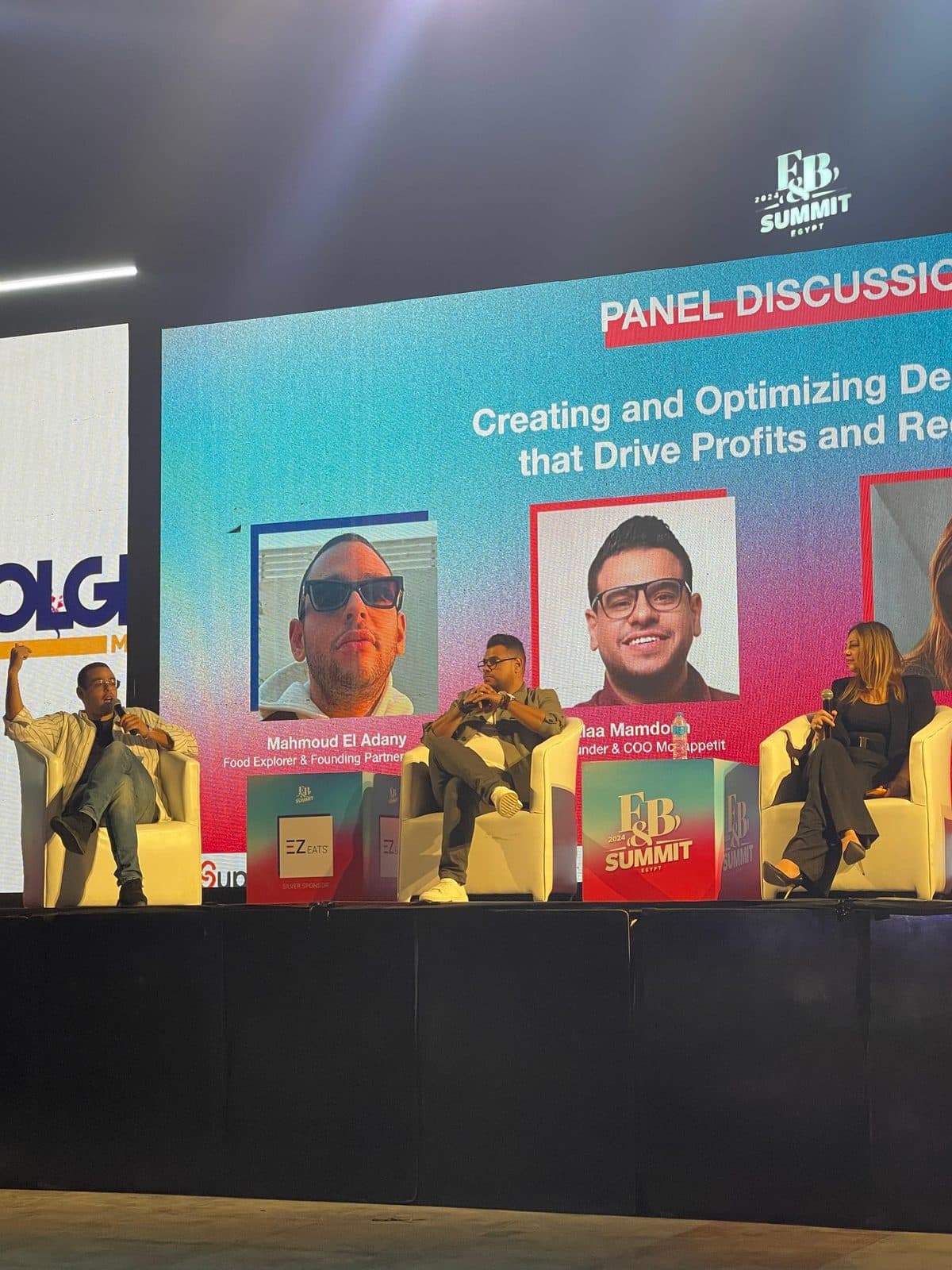 Alaa on a summit panel, seated on stage under a screen reading Panel Discussion