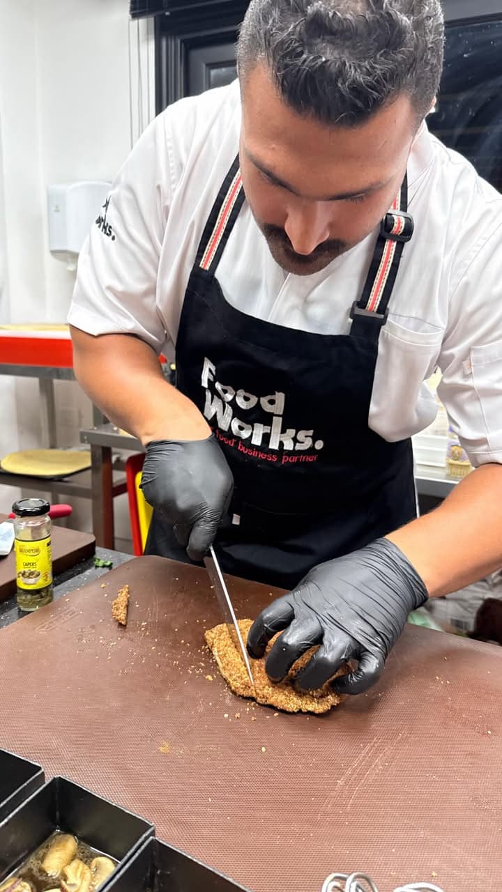 A chef in a Food Works apron working on a dish in the kitchen